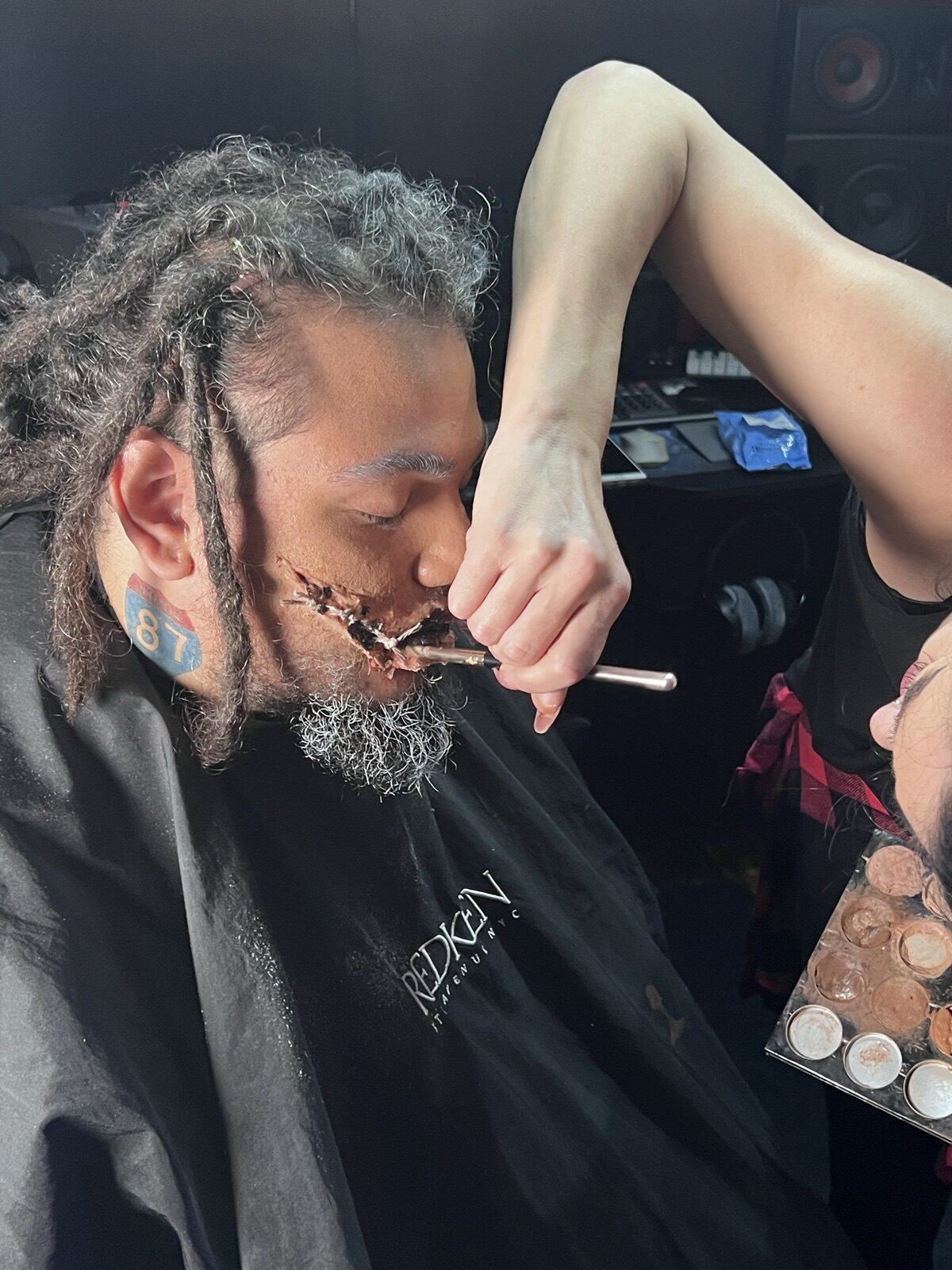 Makeup artist detailing a fictional stitched-mouth effect on an actor for a JGI Media cinema project